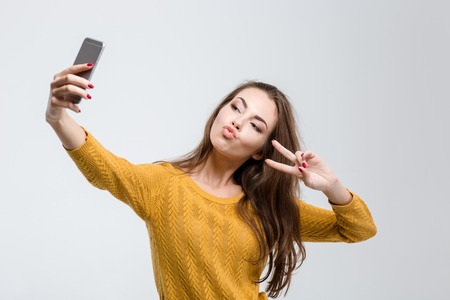 Portrait of a young attractive woman making selfie photo on smartphone isolated on a white background Portrait of a young attractive woman making selfie photo on smartphone isolated on a white background