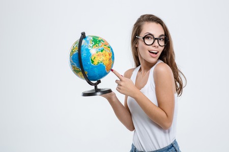 Portrait of a cheerful woman pointing finger on globe and looking at camera isolated on a white...