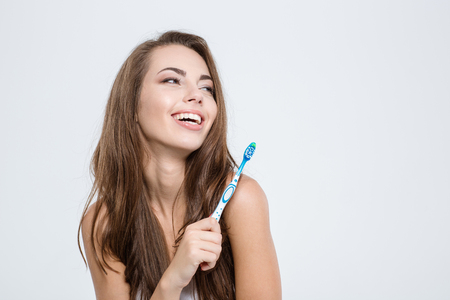 Portrait of a smiling pretty woman holding toothbrush isolated on a white background and looking awayの写真素材