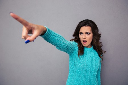 Portrait of a young woman pointing finger on something over gray backgroundの写真素材