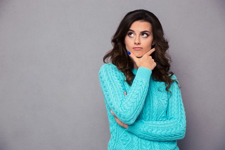 Portrait of a pensive woman standing over gray backgroundの写真素材