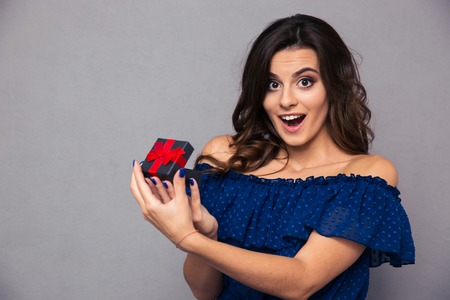 Portrait of a cheerful woman opening jewelry gift box over gray backgroundの写真素材