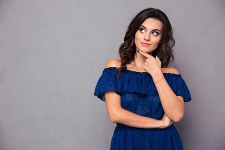 Portrait of a happy thoughtful woman looking away over gray backgroundの写真素材