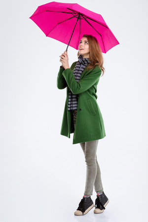 Full length portrait of a smiling woman standing with pink umbrella and looking up isolated on a white backgroundの写真素材