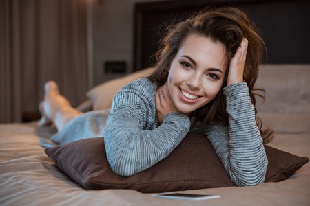 Portrait of a smiling pretty woman lying on the bed and looking at cameraの写真素材
