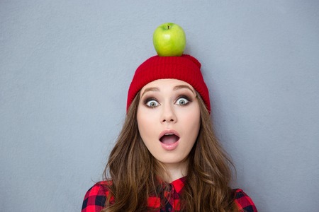 Portrait of a young woman with apple on head looking at camera over gray backgroundの写真素材