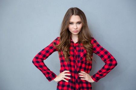 Angry young beautiful curly woman in checkered shirt c standing with arms akimboの写真素材