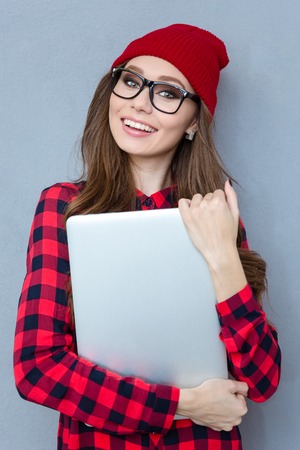 Portrait of a smiling hipster woman holding laptop computer over gray background and looking at cameraの写真素材