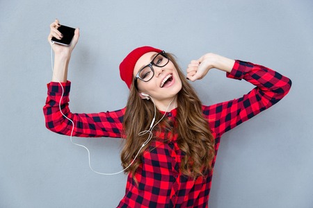 Portrait of a happy woman listening music in headphones and dancing over gray backgroundの写真素材
