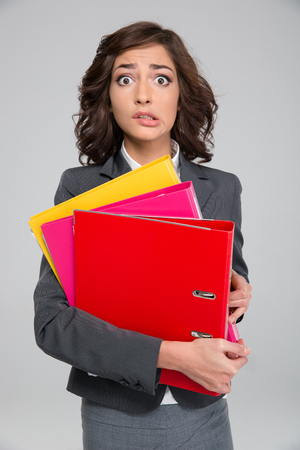 Young curly stressed shocked business woman biting bottom lip holding colorful foldersの写真素材