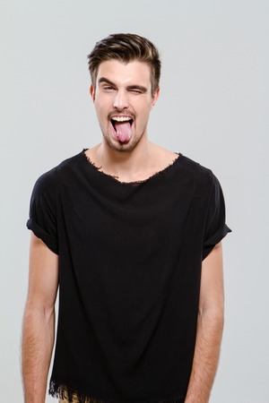 Young funny handsome guy in black t-shirt winking and sticking out his tongue