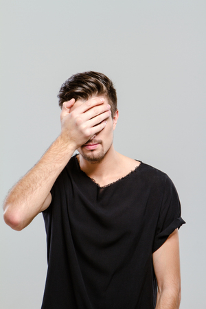 Young handsome man doing facepalm covering his eyes and face with palmの写真素材
