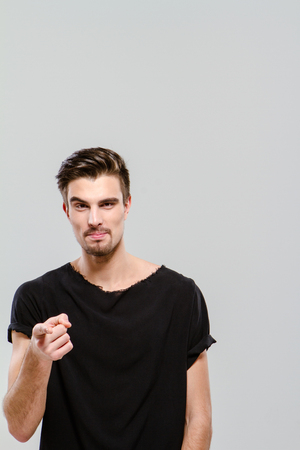 Young handsome charming guy in black t-shirt pointing on youの写真素材