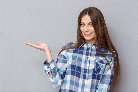 Portrait of a smiling woman holding copyspace on the palm over gray backgroundの写真素材