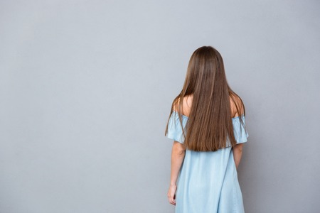 Back view of young woman with long hair in blue dress standing on gray backgroundの写真素材