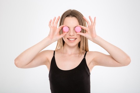 Pretty young woman put macarons instead of eyes and look at cameraの写真素材