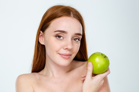 Beauty portrait of a attractive redhair woman with skincare holding apple isolated on a white backgroundの写真素材