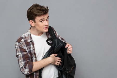 Portrait of a young male student pulls out something of backpack over gray backgroundの写真素材