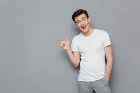 Portrait of handsome inspired attractive casual male in white t-shirt and gray pants pointing away...