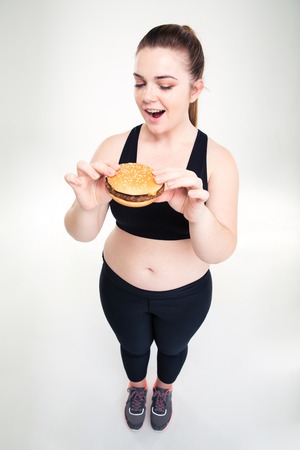 Full length portrait of a fat woman eating burger isolated on a white background