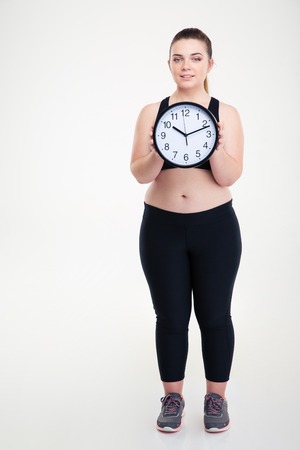Full length portrait of a smiling fat woman holding wall clock isolated on a white backgroundの写真素材