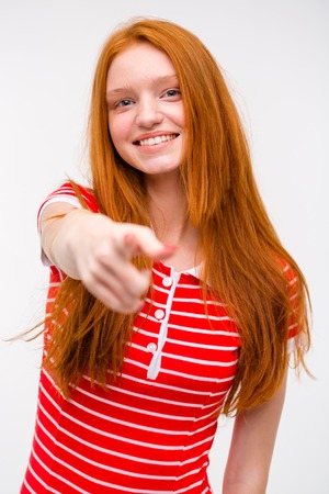 Beautiful cheerful joyful redhead teenager red striped t-shirt pointing at the camera on a white isolated backgroundの写真素材