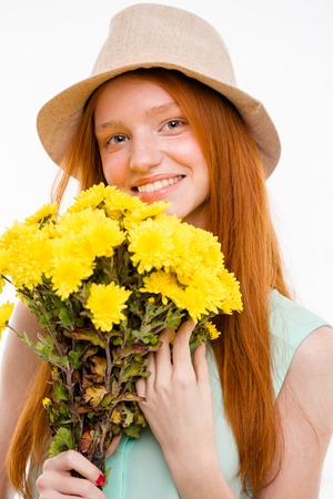 Portrait of happy cheerful pretty natural girl with long red hair in boonie hat holding flowersの写真素材