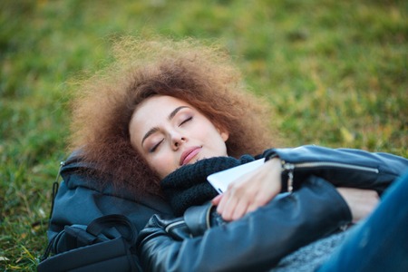 Portrait of a young woman with curly hair sleeping on green grass outdoorsの写真素材