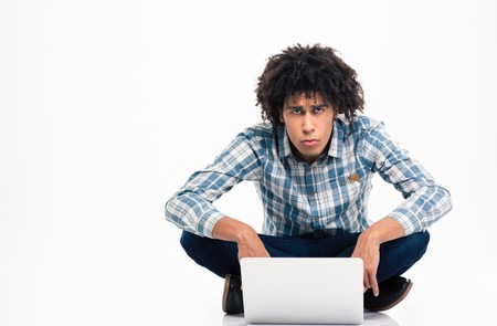 Sad afro american man sitting on the floor with laptop computer and looking at camera isolated on a...