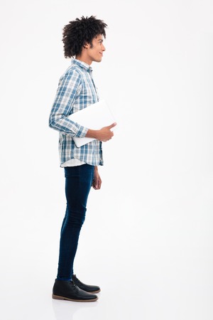 Side view portrait of a happy afro american man standing with laptop computer isolated on a white backgroundの写真素材