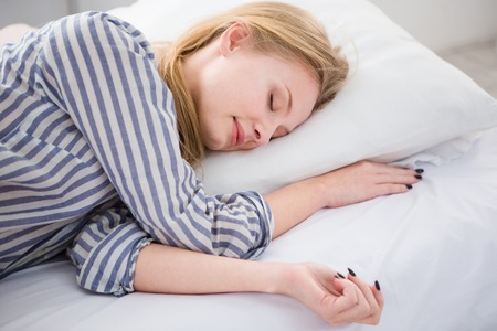 Pretty blonde young woman sleeping in her white bed on the pillow in striped pajamasの写真素材