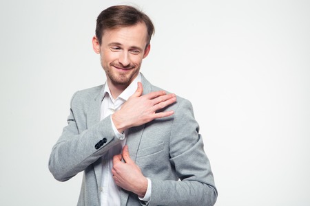 Portrait of a smiling businessman cleaning jacket with hand isolated on a white backgroundの写真素材