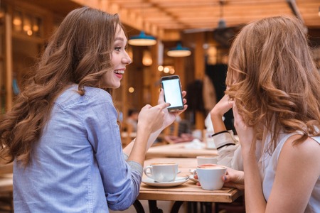Portrait of a smiling woman showing something on smartphone screen to her girlfriends in cafe