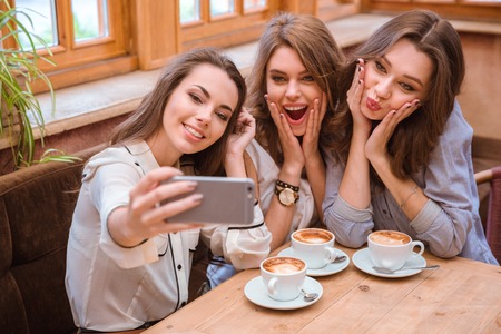 Portrait of a young three women making selfie photo on smartphone in cafeの写真素材