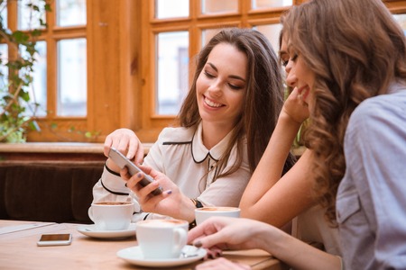 Portrait of a smiling three women using smartphone in cafe togetherの写真素材