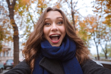 Portrait of a beautiful cheerful woman making selfie photo in autumn park