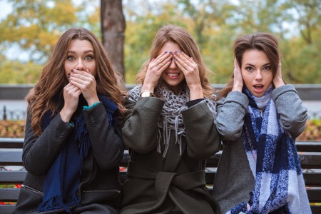 Portrait of a three women sitting on the bench and representing senses: mute, blind and deaf outdoorsの写真素材