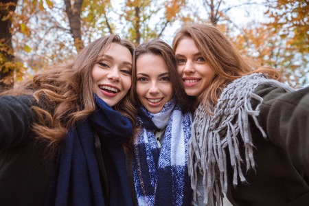 Portrait of a happy three girlfriends making selfie photo on camera outdoors