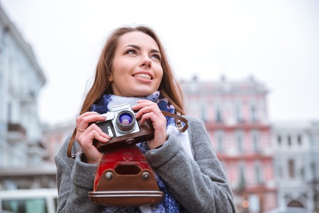 Portrait of a smiling young woman holding retro camera and looking away outdoors