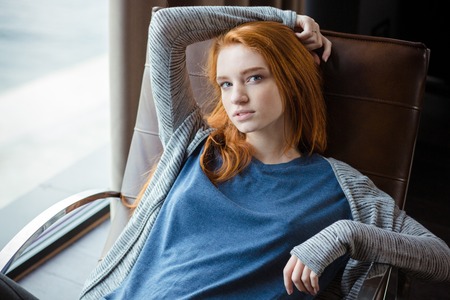 Portrait of a beautiful redhead woman relaxing on rocking chair at homeの写真素材
