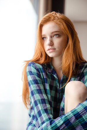 Portrait of thoughtful beautiful redhead young lady in checkered shirt looking awayの写真素材
