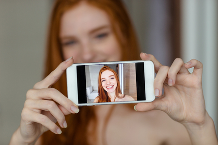 Portrait of a happy redhead woman making selfie photo on smartphoneの写真素材