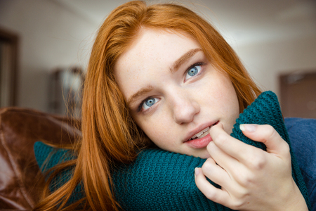 Thoughtful attractive redhead young lady hugging knitted pillowの写真素材
