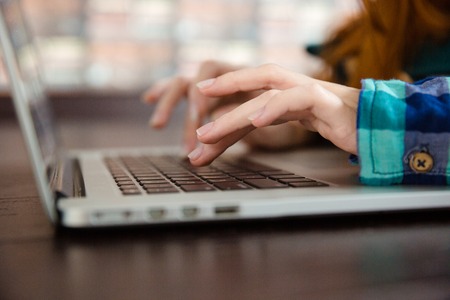 Hands of young woman in checkered shirt typing using laptopの写真素材