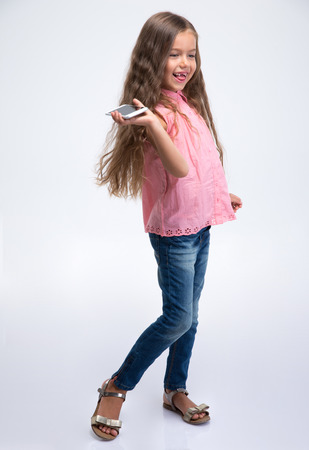 Full length portirat of a little girl holding smartphone isolated on a white backgroundの写真素材