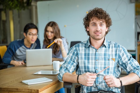 Attractive cheerful young curly male in checkered shirt studying with students in classroomの写真素材