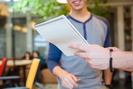 Closeup of male hand showing his notes to young cheerful guyの写真素材