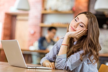 Attractive relaxed curly young woman sitting in cafe with closed eyes, smiling and dreamingの写真素材
