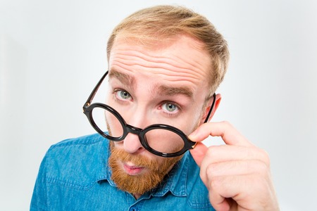 Closeup portrait of amusing young man with beard looking over black round glasses isolated over white backgroundの写真素材