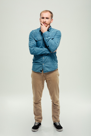 Full length portrait of a casual pensive man standing isolated on a white backgroundの写真素材